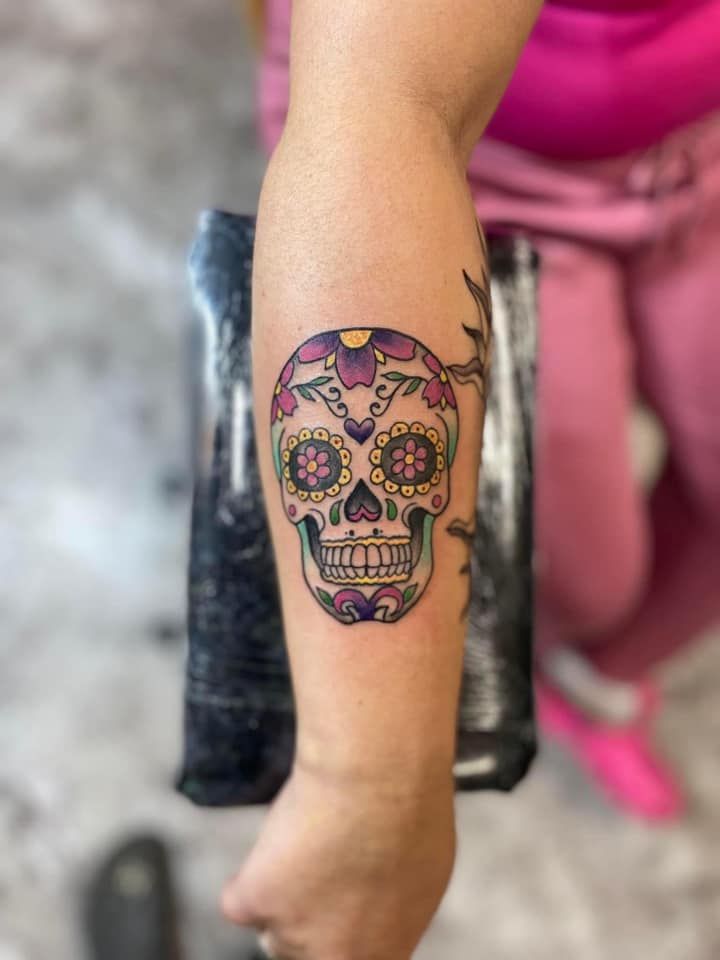 A woman has a sugar skull tattoo on her forearm.