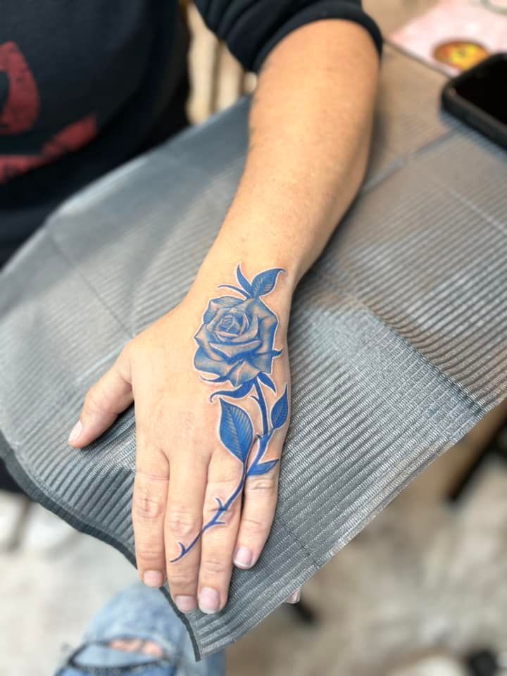 A woman has a blue rose tattoo on her hand.