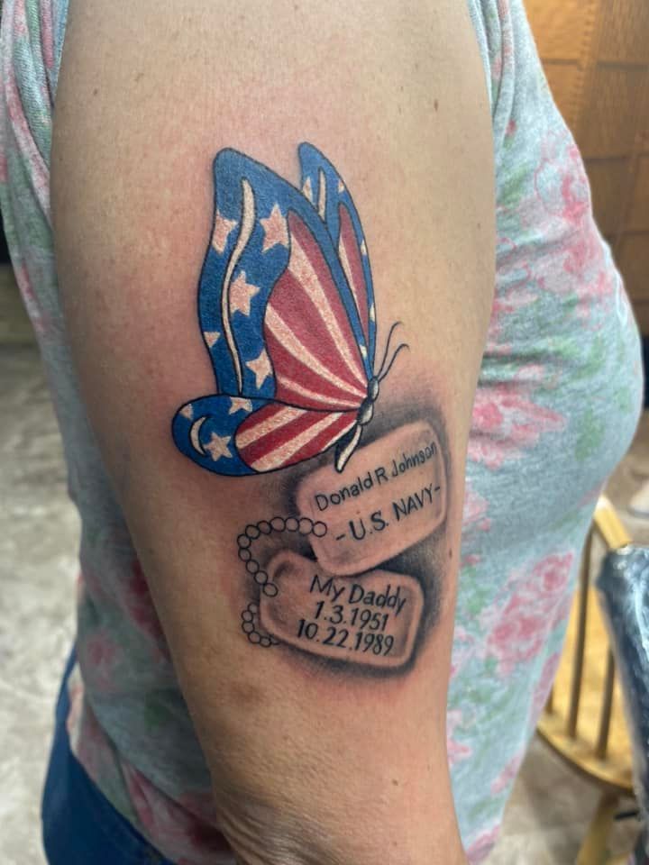 A woman has a tattoo of a butterfly and dog tags on her arm.