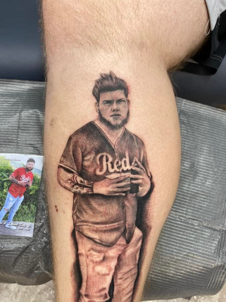 A man has a tattoo of a man in a reds jersey on his leg.