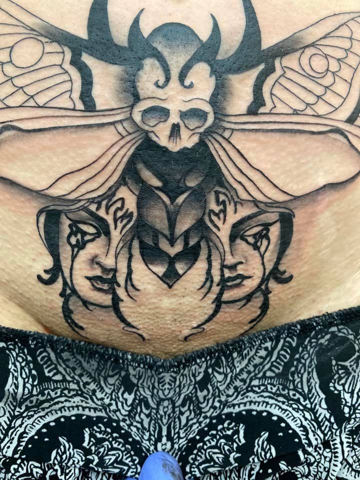 A woman has a tattoo of a beetle with three faces on her stomach.