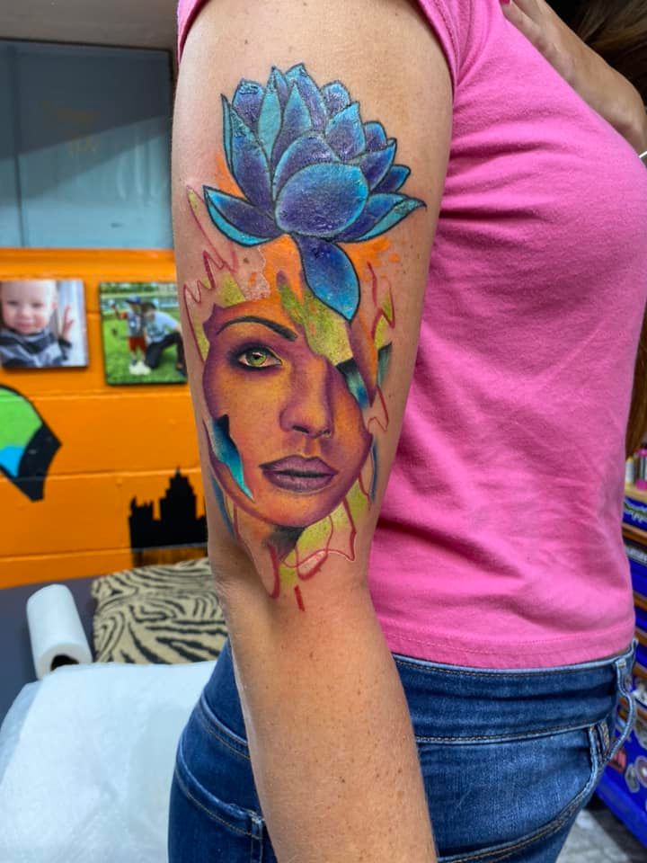 A woman has a tattoo of a woman 's face and a flower on her arm
