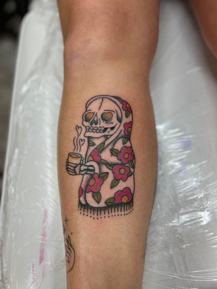 A tattoo of a skeleton holding a cup of coffee on a person 's leg.