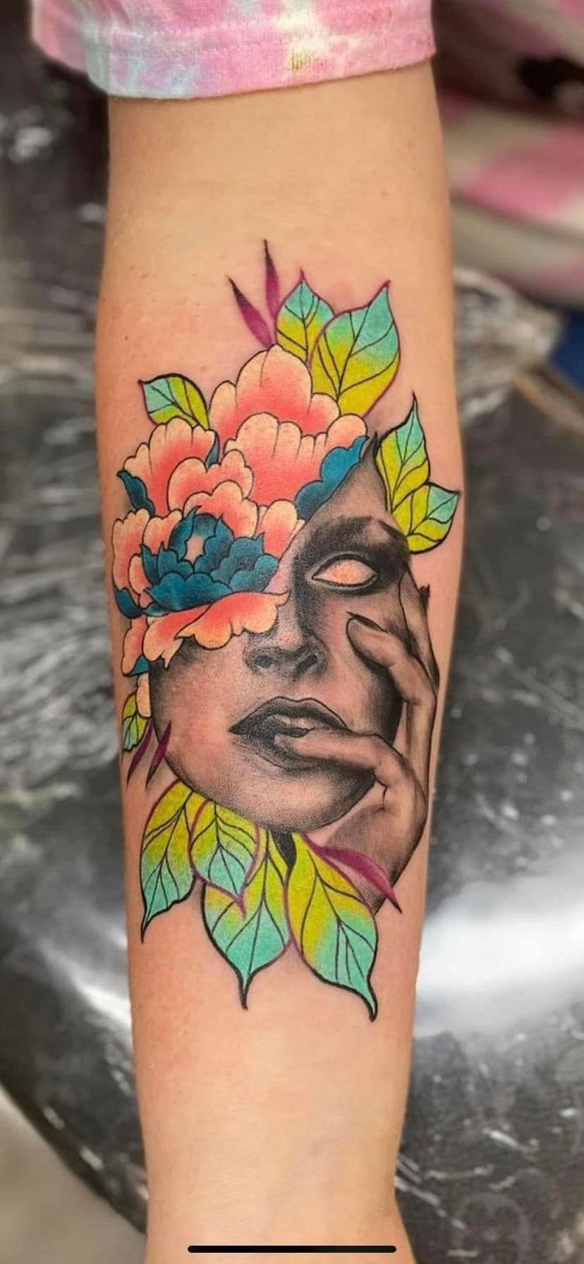 A tattoo of a woman 's face with flowers and leaves on her forearm.