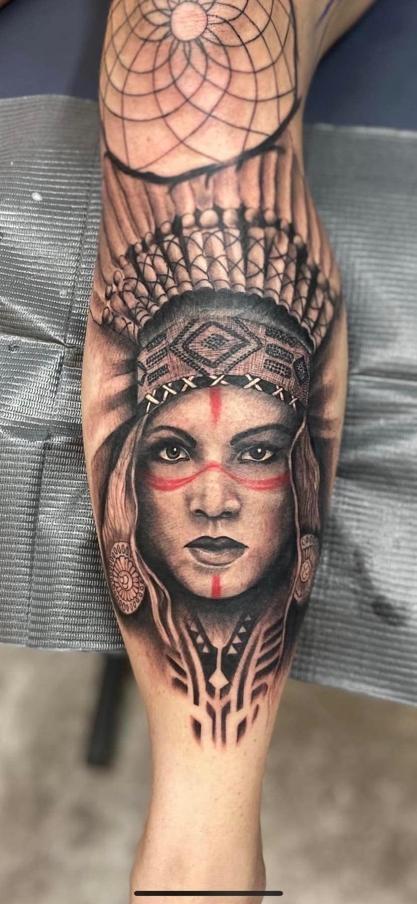 A tattoo of a native american woman with a dream catcher on her leg.