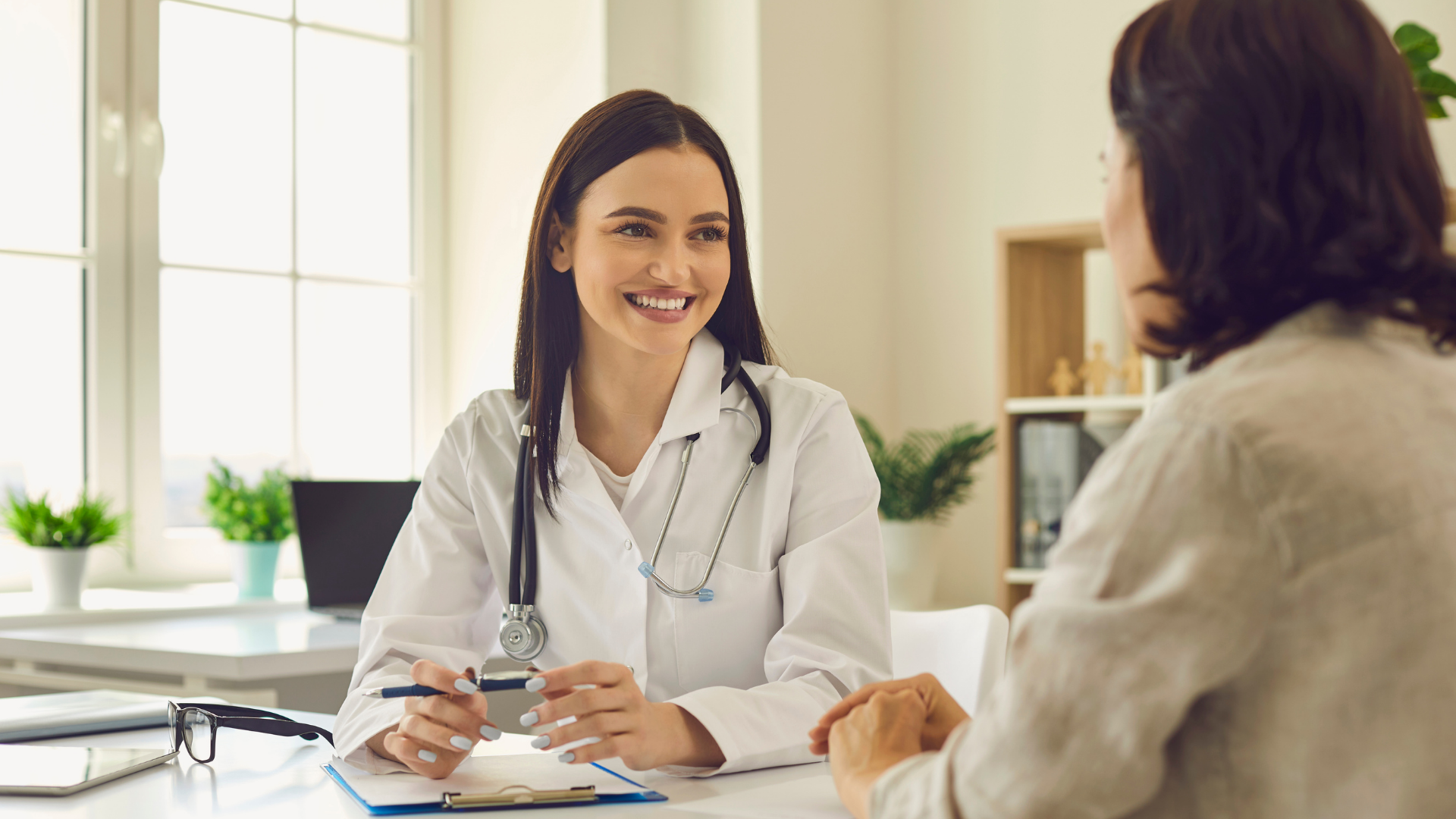 A female doctor is sitting at a desk talking to a patient.