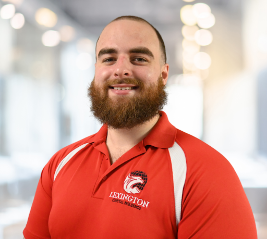 Man with beard wearing a red polo shirt with Lexington Canine Academy logo, smiling.