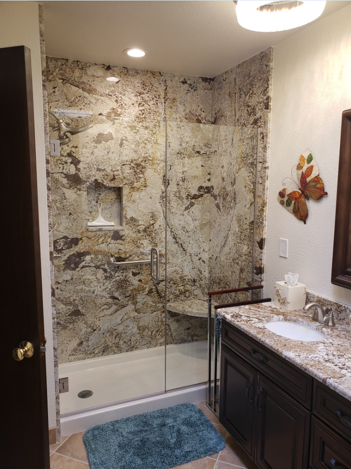 Bathroom with granite vanity, shower-tub, and stone-look tile walls.