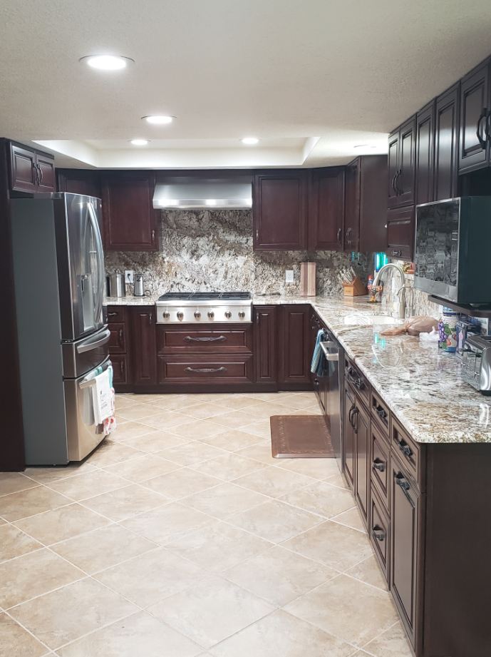 Modern kitchen with dark wood cabinets, granite counters, stainless appliances, and tan tile floor.