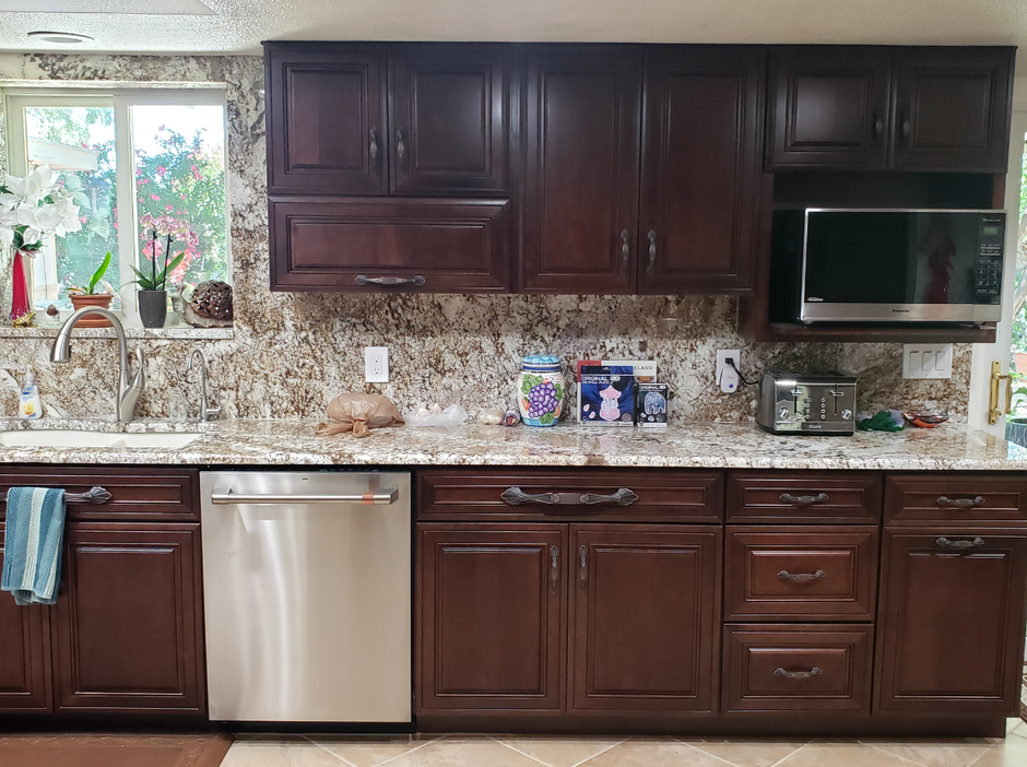 Modern kitchen with dark wood cabinets, granite countertop, stainless dishwasher, and a window over the sink.