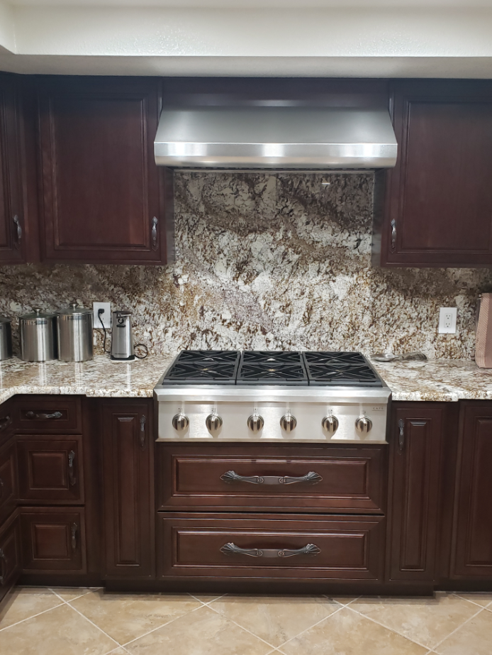 Dark wood kitchen with stainless steel range, granite backsplash, and under-cabinet hood.