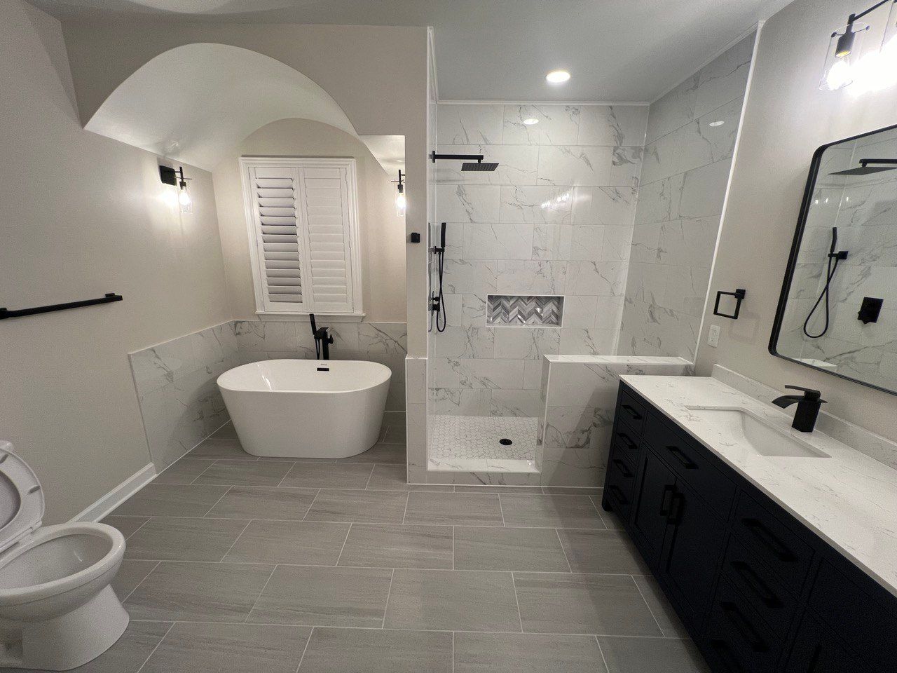 Master bathroom in Ellicott City with double vanity, large walk-in shower, freestanding tub, and arched ceiling