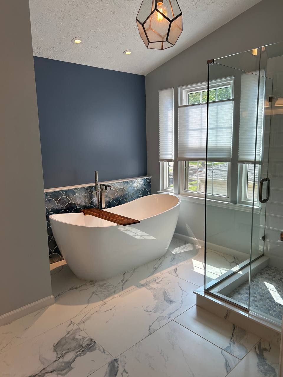 Modern bathroom remodel in Parkville, MD featuring a freestanding tub, glass walk-in shower, white marble-look tile, and navy blue accent wall.