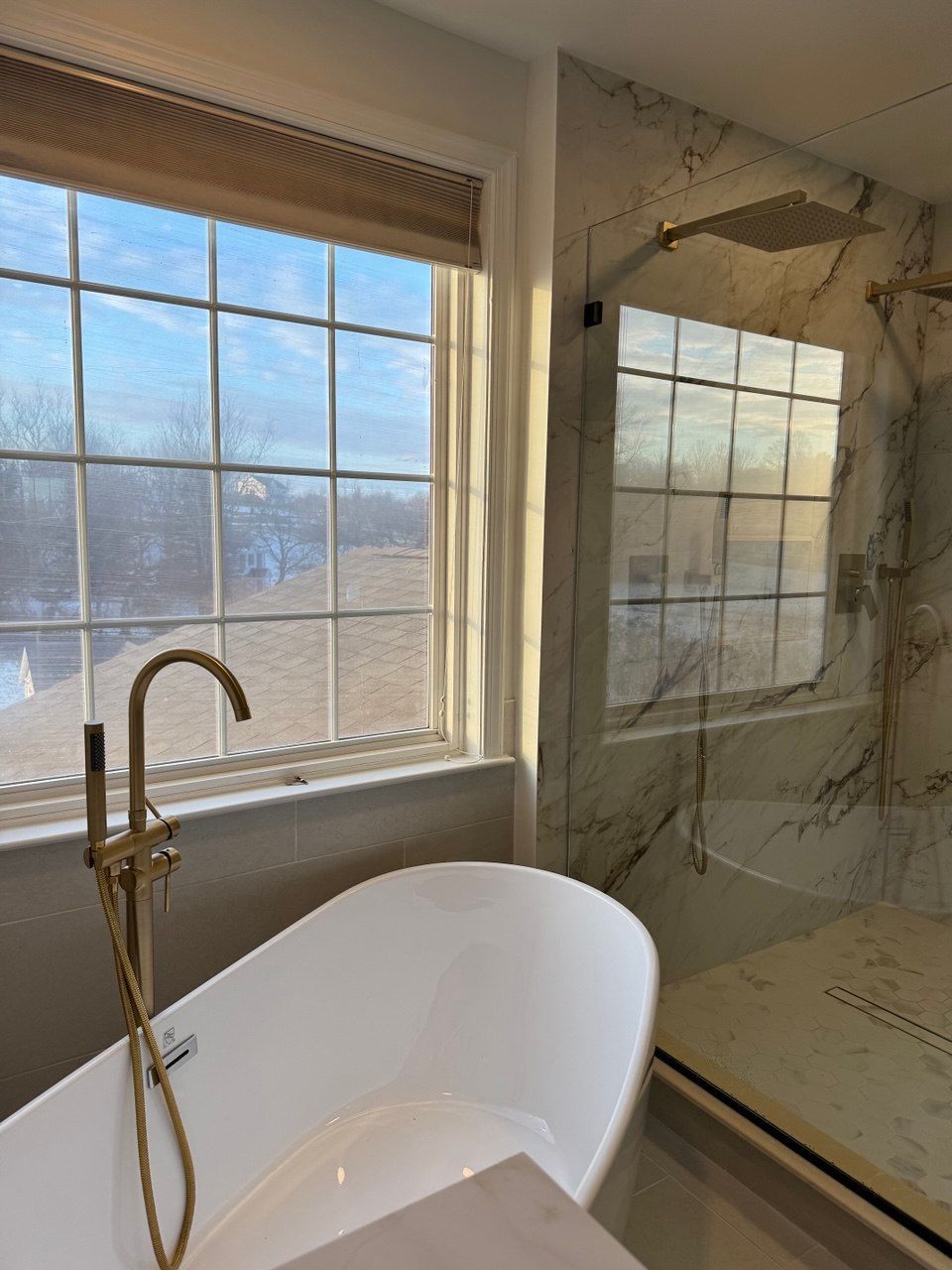 Large master bathroom in Westminster with freestanding tub, heated floors, double vanity with makeup space, large shower tile, brushed gold mirrors, and sconces