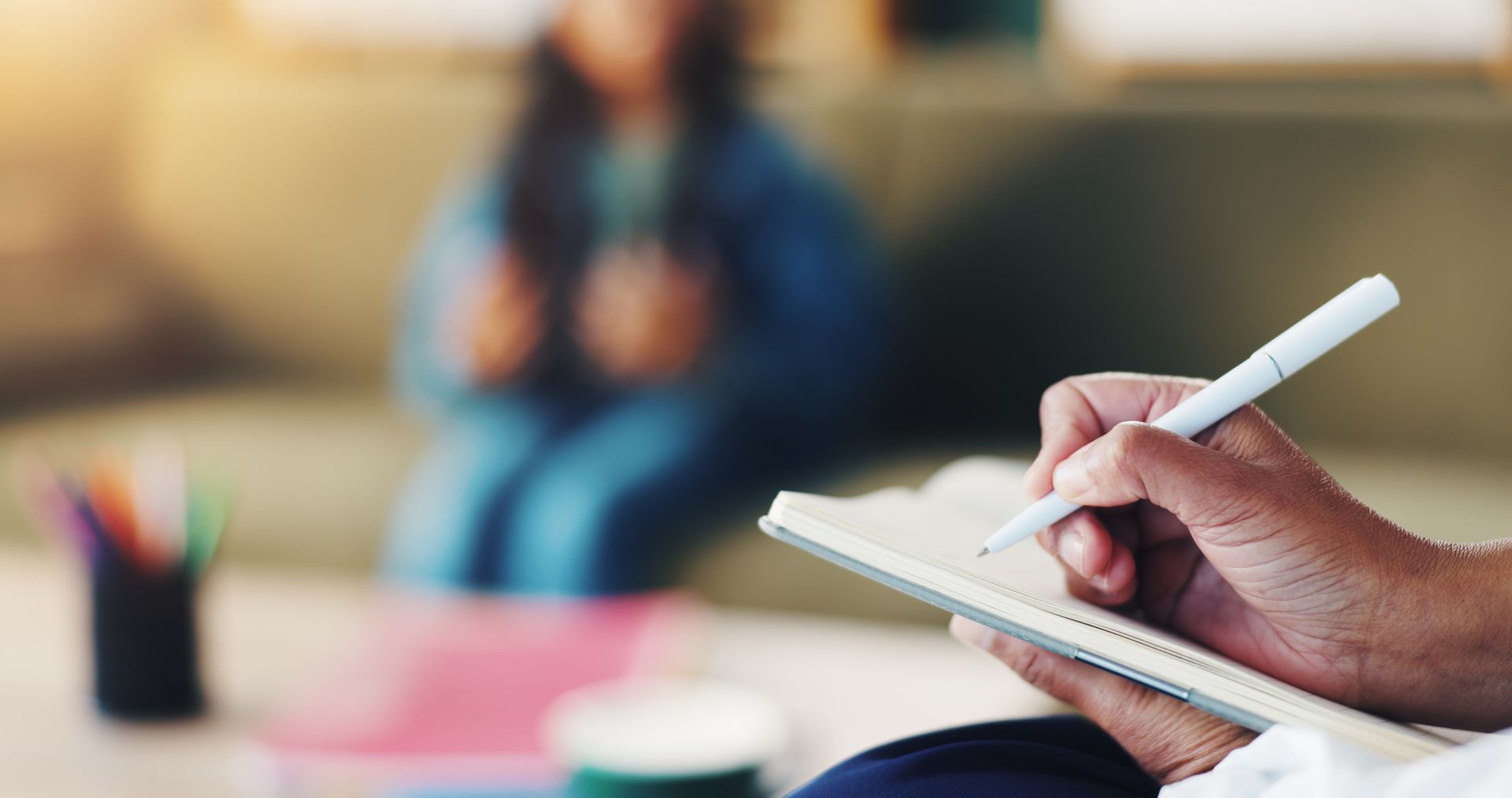 A therapist is taking notes on a clipboard during a child counseling session in an office.