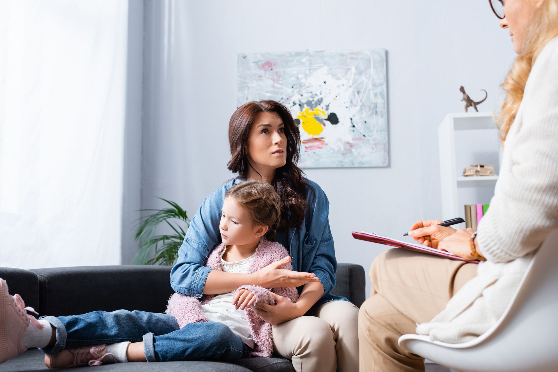 A counselor is taking notes during a family therapy session with an adult and a child
