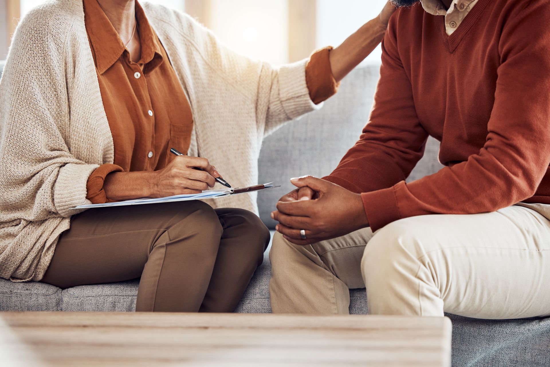 Counselor comforting a client while taking notes during a conversation on a sofa. Counselor comforting a client while taking notes during a conversation on a sofa.