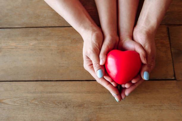 A woman and child are holding a red heart in their hands.