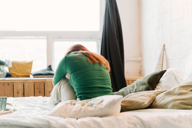 A woman is sitting on a bed with her head on her knees.