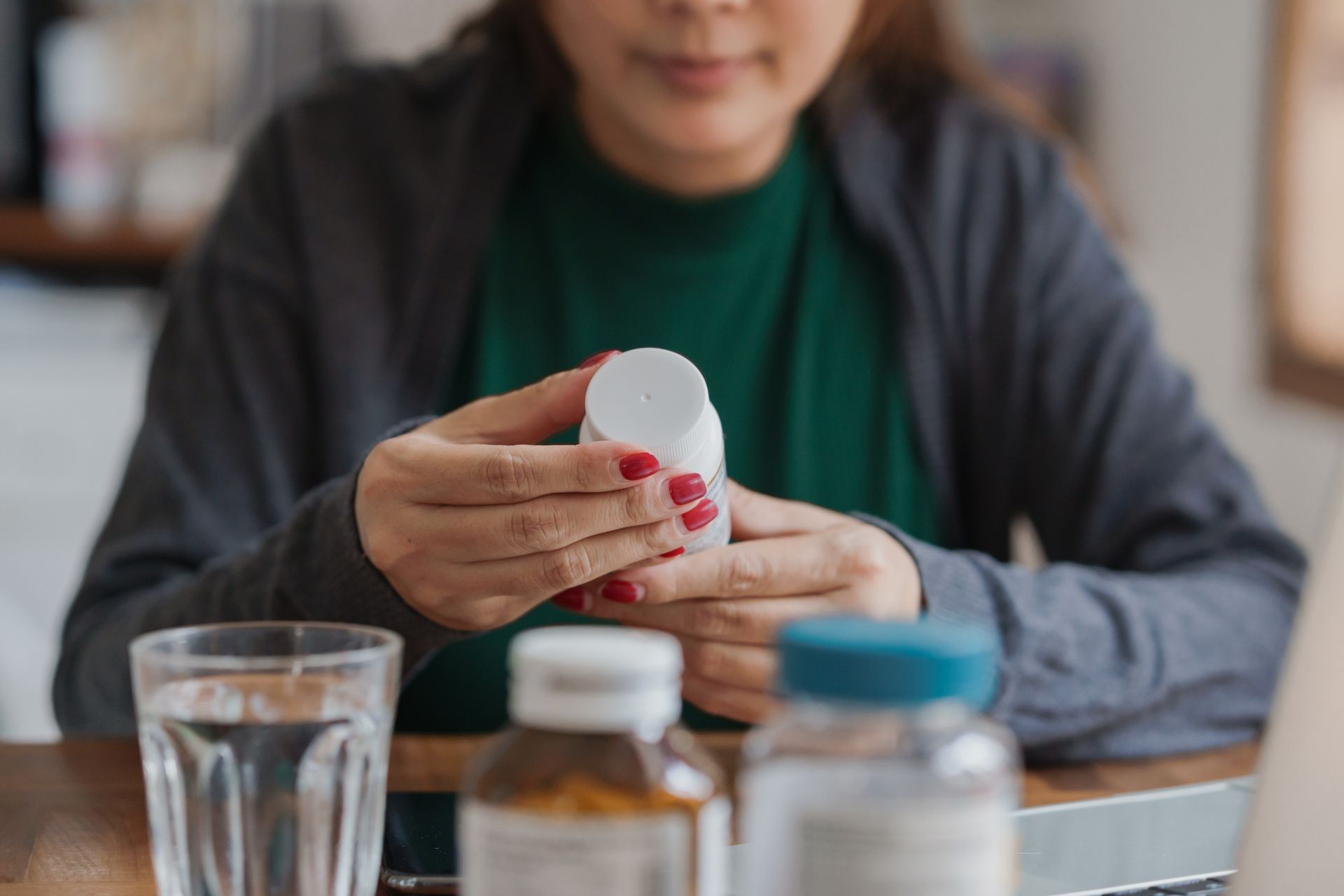 A woman is sitting at a table holding a bottle of pills.