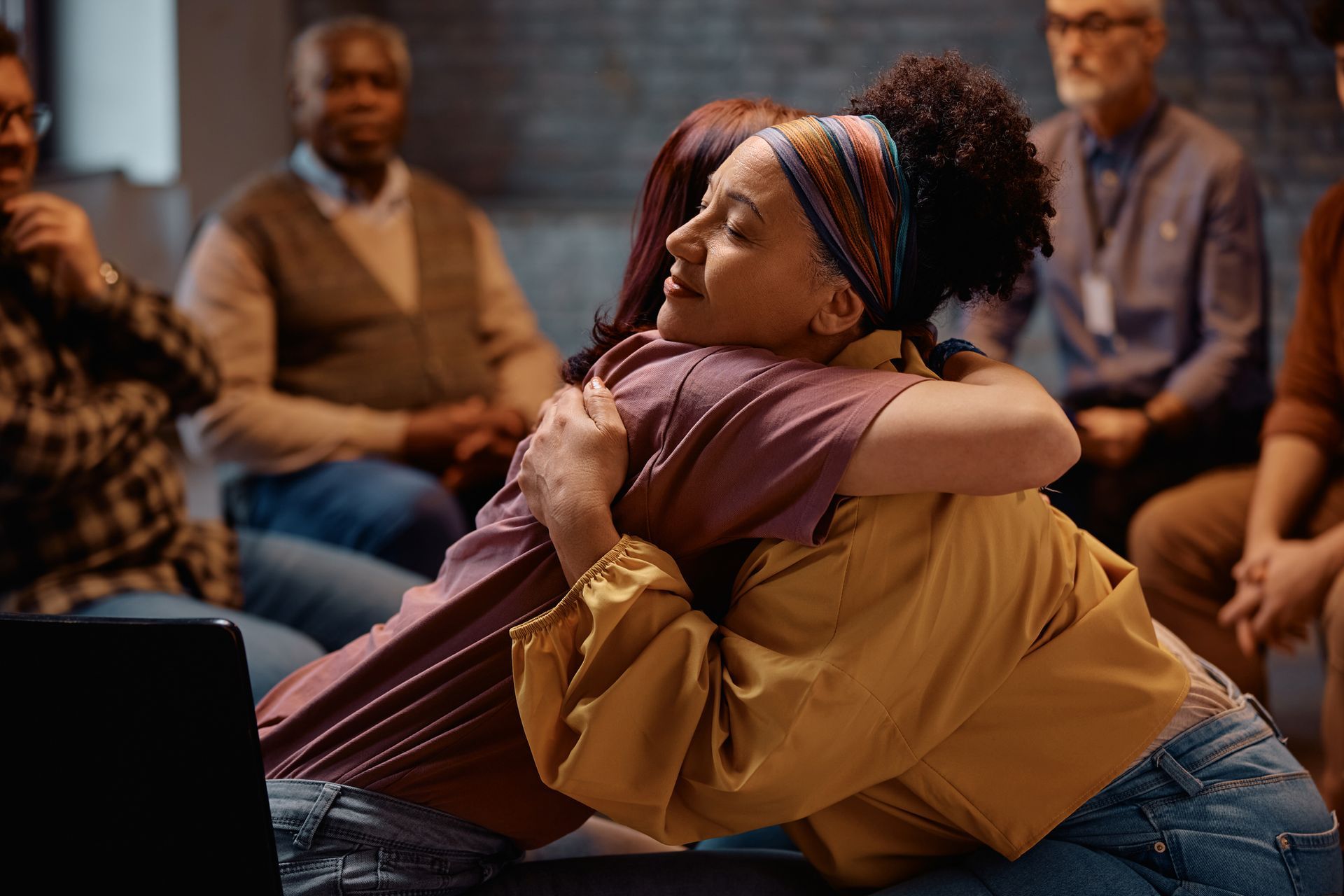 A group of people are sitting around a table hugging each other. A group of people are sitting around a table hugging each other.