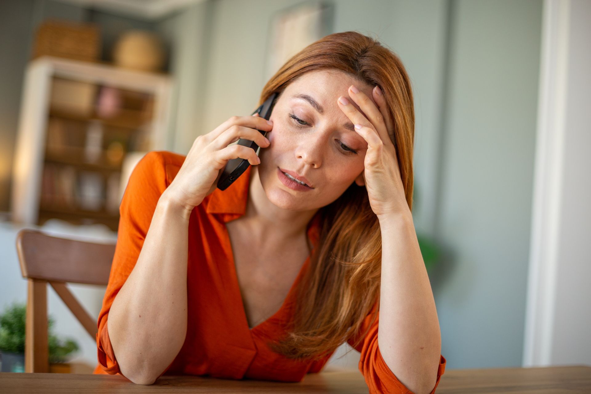 A woman is sitting at a table talking on a cell phone.