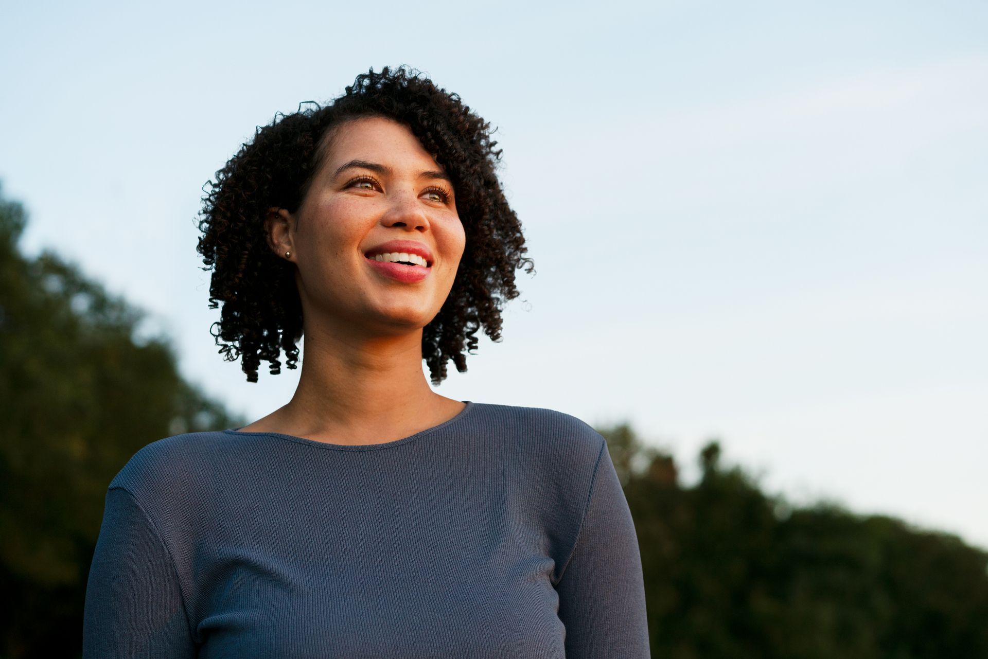 A young black woman viewed from the front, looking at a sunset and smiling.