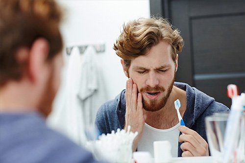 man notices dental pain while brushing teeth