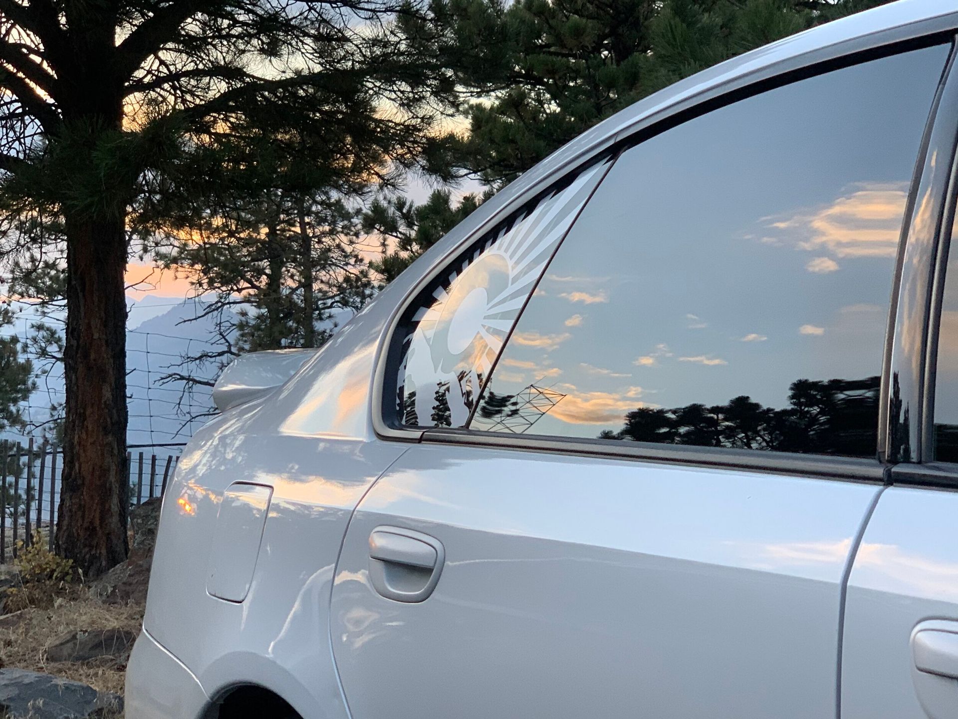 A silver car is parked in front of a lake with trees in the background.