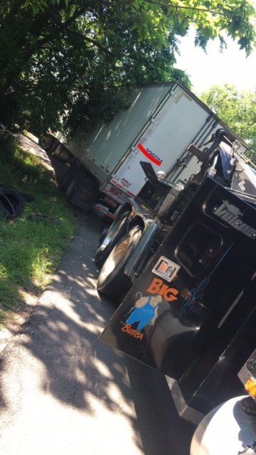 Semi-truck tilted on its side on a road next to grass and trees; the truck has a 