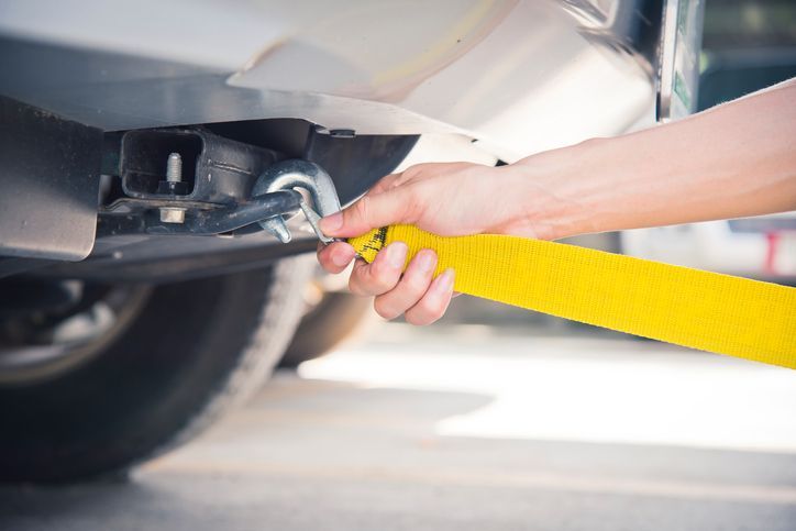 Close-up of black car being towed with a yellow towing rope with a silver hook.