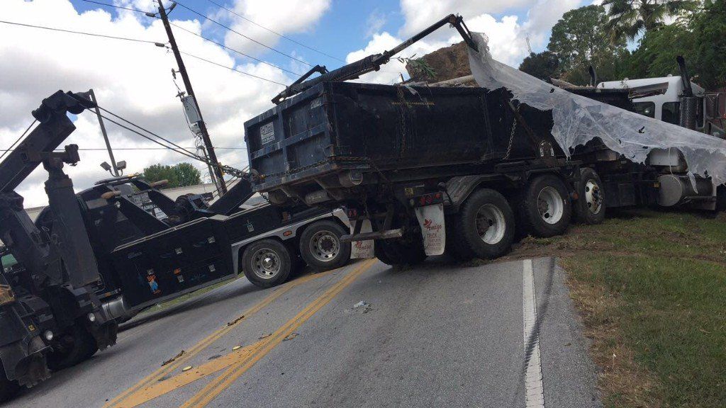 A tow truck attempting to upright a tipped-over dump truck on a road.