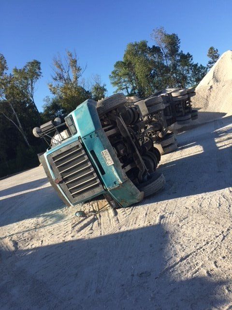 A turquoise truck overturned on its side in a gravel pit with a pile of rocks nearby.