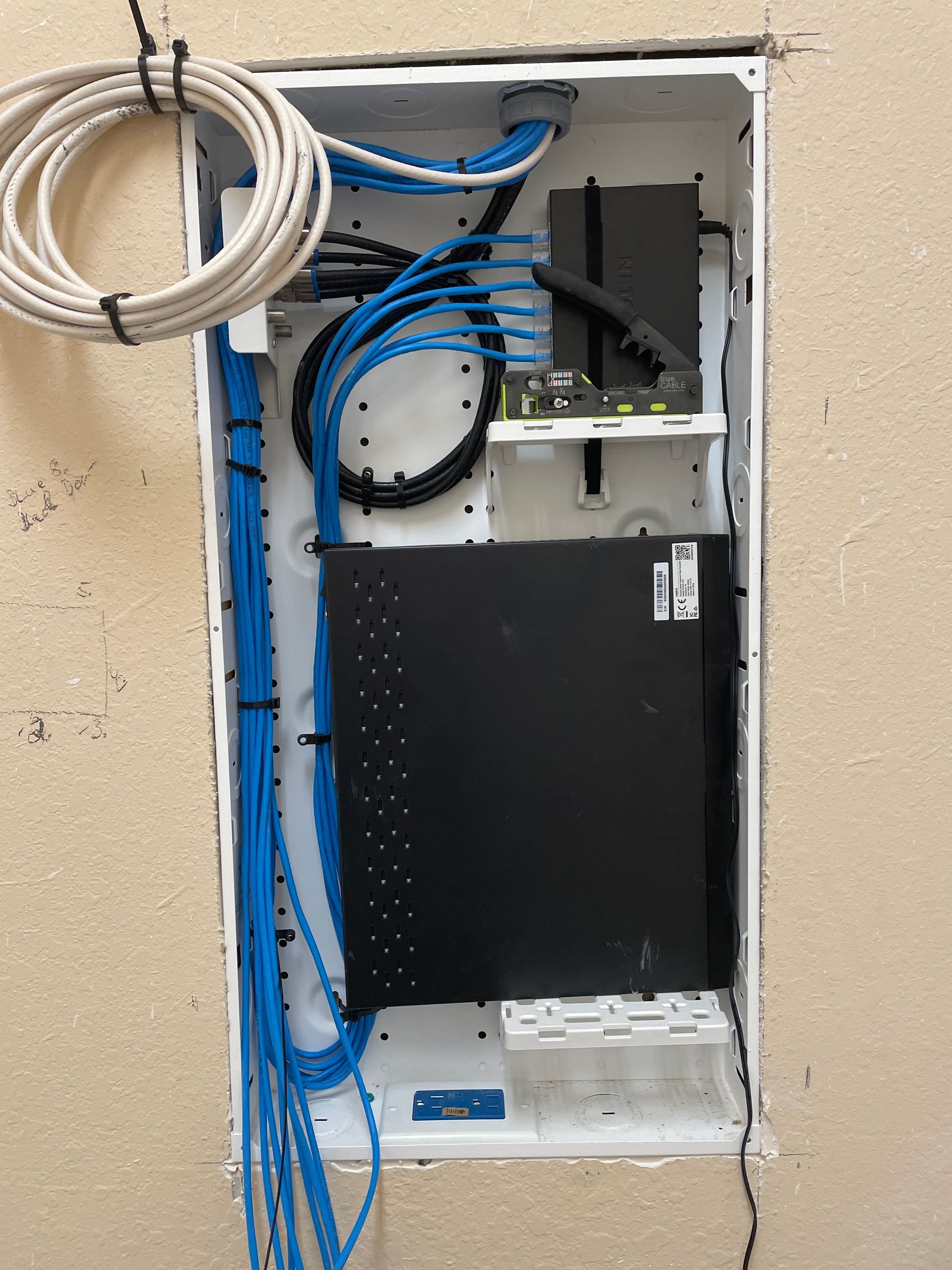 A white wall-mounted network enclosure with blue and white cables, and a black network device installed.