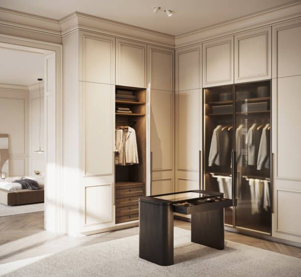 Walk-in closet with custom built-ins in a light color. A dark vanity sits in the foreground, bedroom visible in the background.