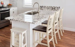 Kitchen island with granite countertop, sink, and four white chairs with brown seats. A white step stool is in front.