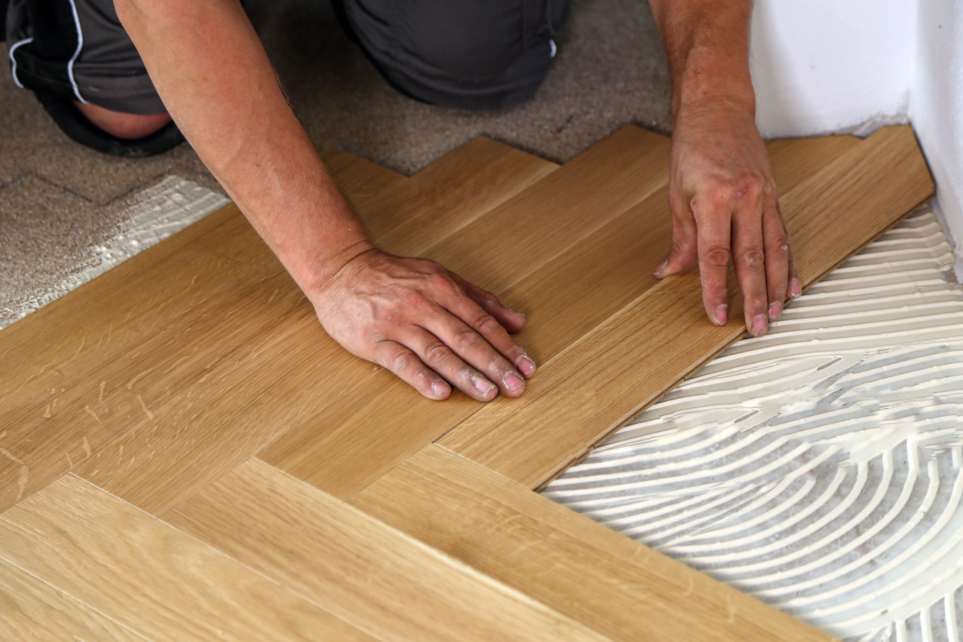 Person installing herringbone pattern wood flooring with glue.