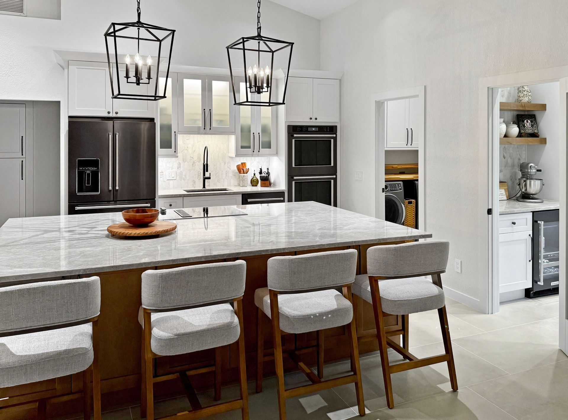 Modern kitchen with island, seating, dark appliances, white cabinets, and pendant lights.