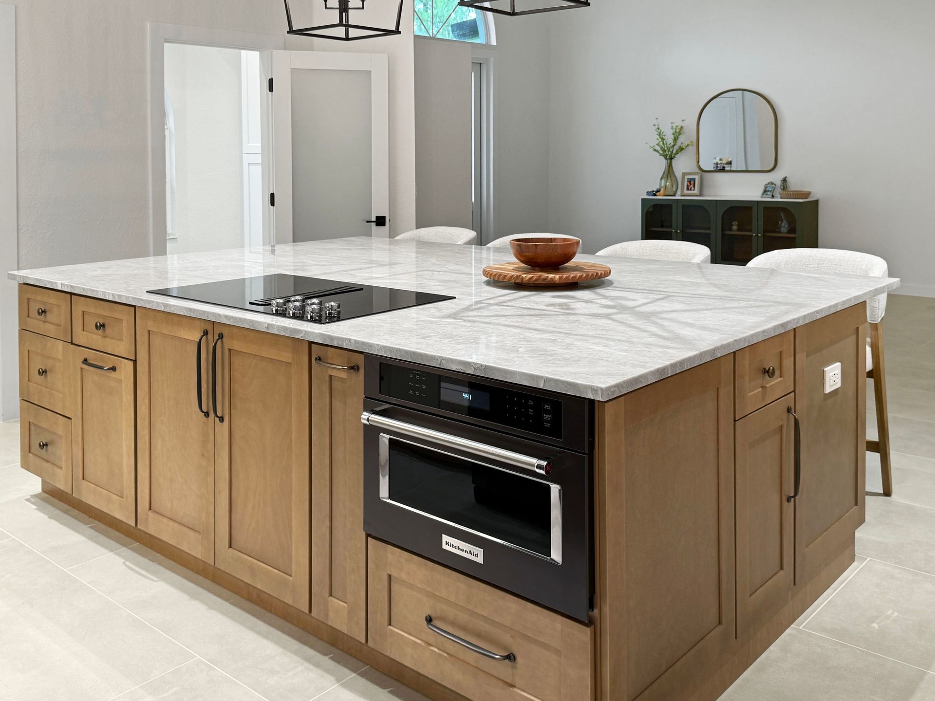 Kitchen island with light countertops and wood cabinets. Built-in microwave, cooktop, and seating area.