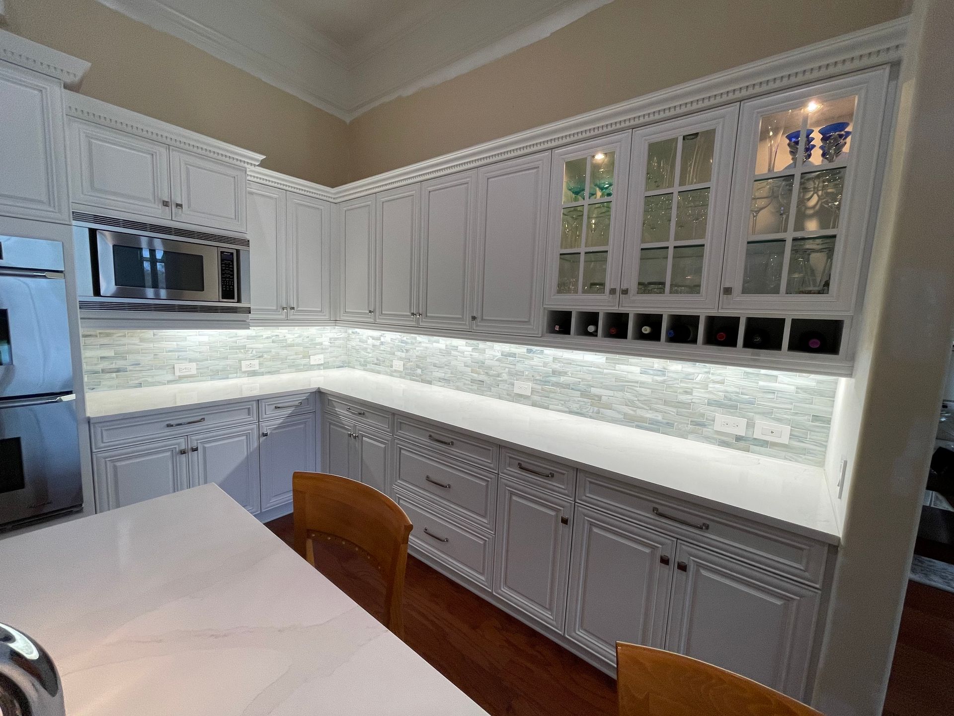 White kitchen cabinets with countertop and a few wooden chairs.