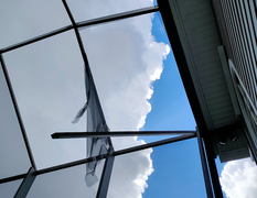 Sky visible through a damaged screened-in porch roof, with torn sections and metal framing.