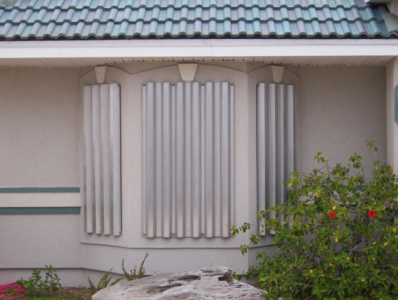 Exterior of a building with corrugated metal hurricane shutters covering a window, green roof.