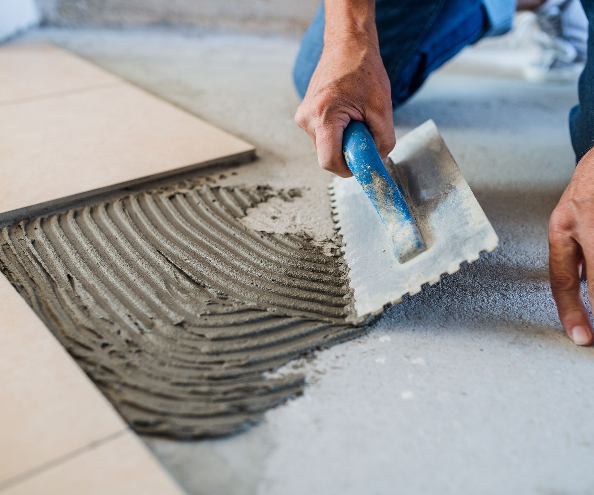 Person using a notched trowel to spread mortar on a floor for tile installation.