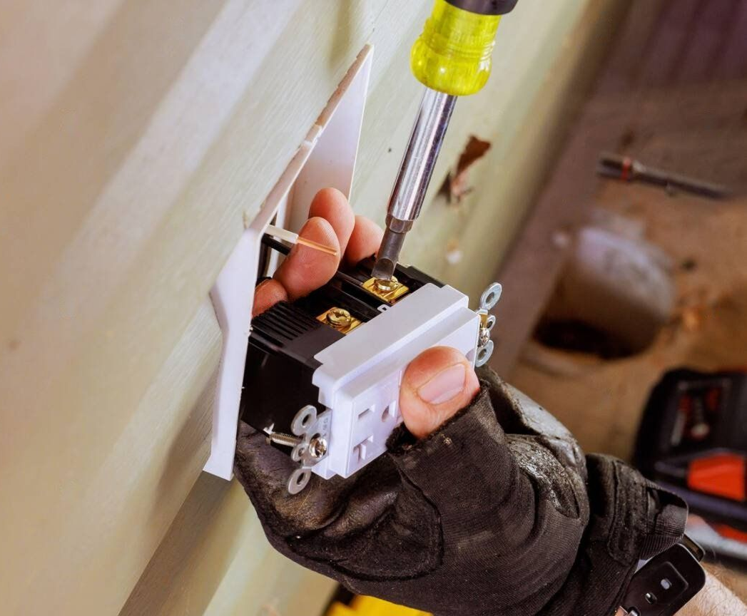 Person in work gloves installing an electrical outlet with a screwdriver.