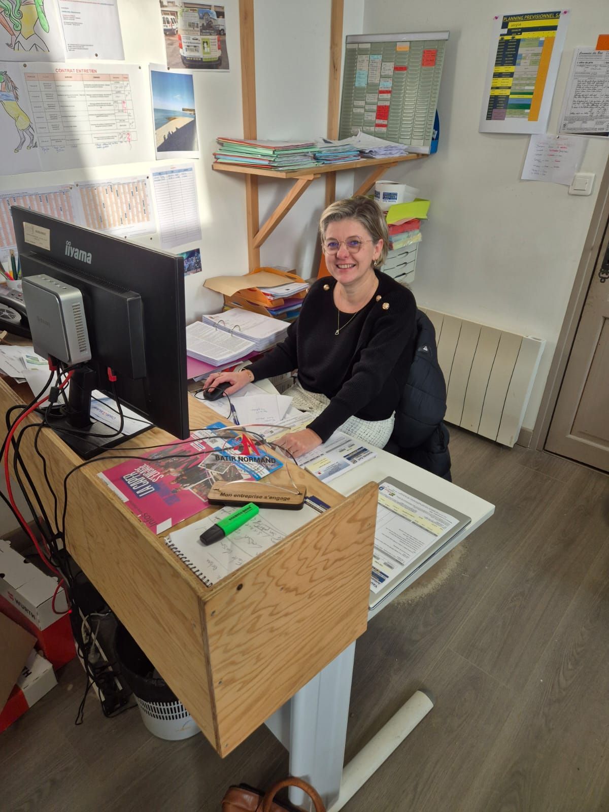 Femme souriante à son bureau, travaillant sur un ordinateur dans un environnement de bureau.