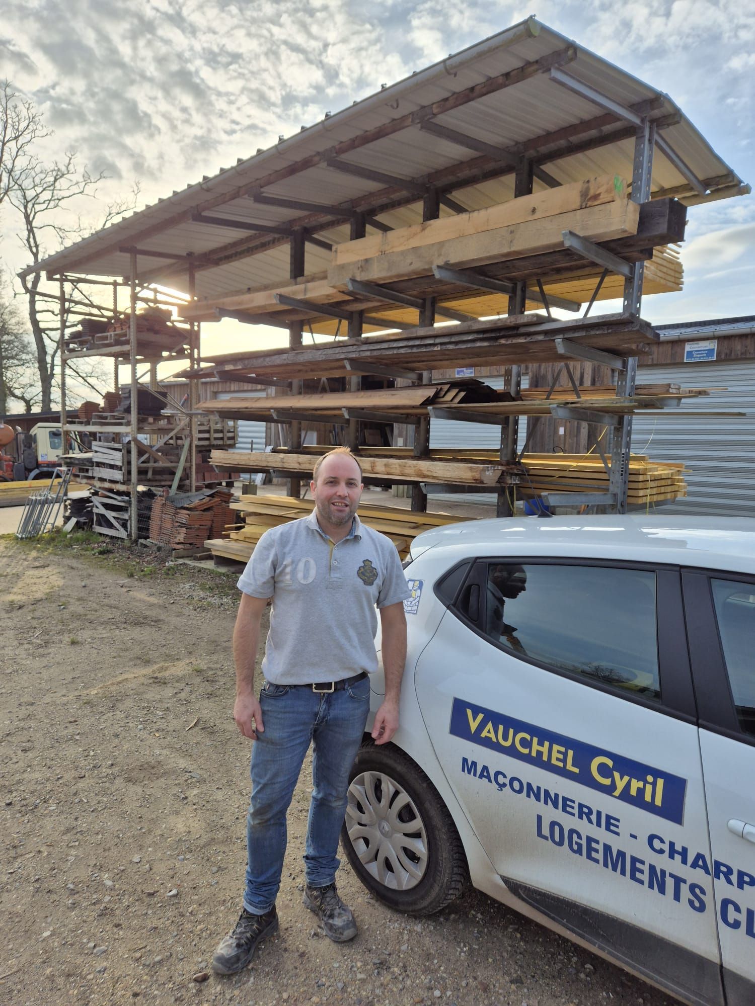 Un homme se tient debout près d'une voiture arborant le logo de l'entreprise, à côté d'un râtelier à bois extérieur.