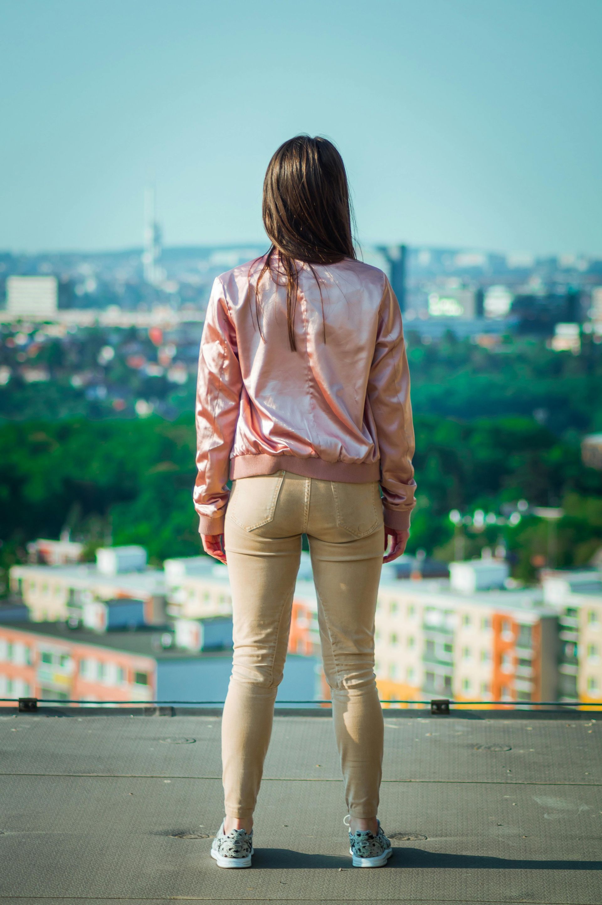 Une femme en veste rose et pantalon beige contemple le paysage urbain.