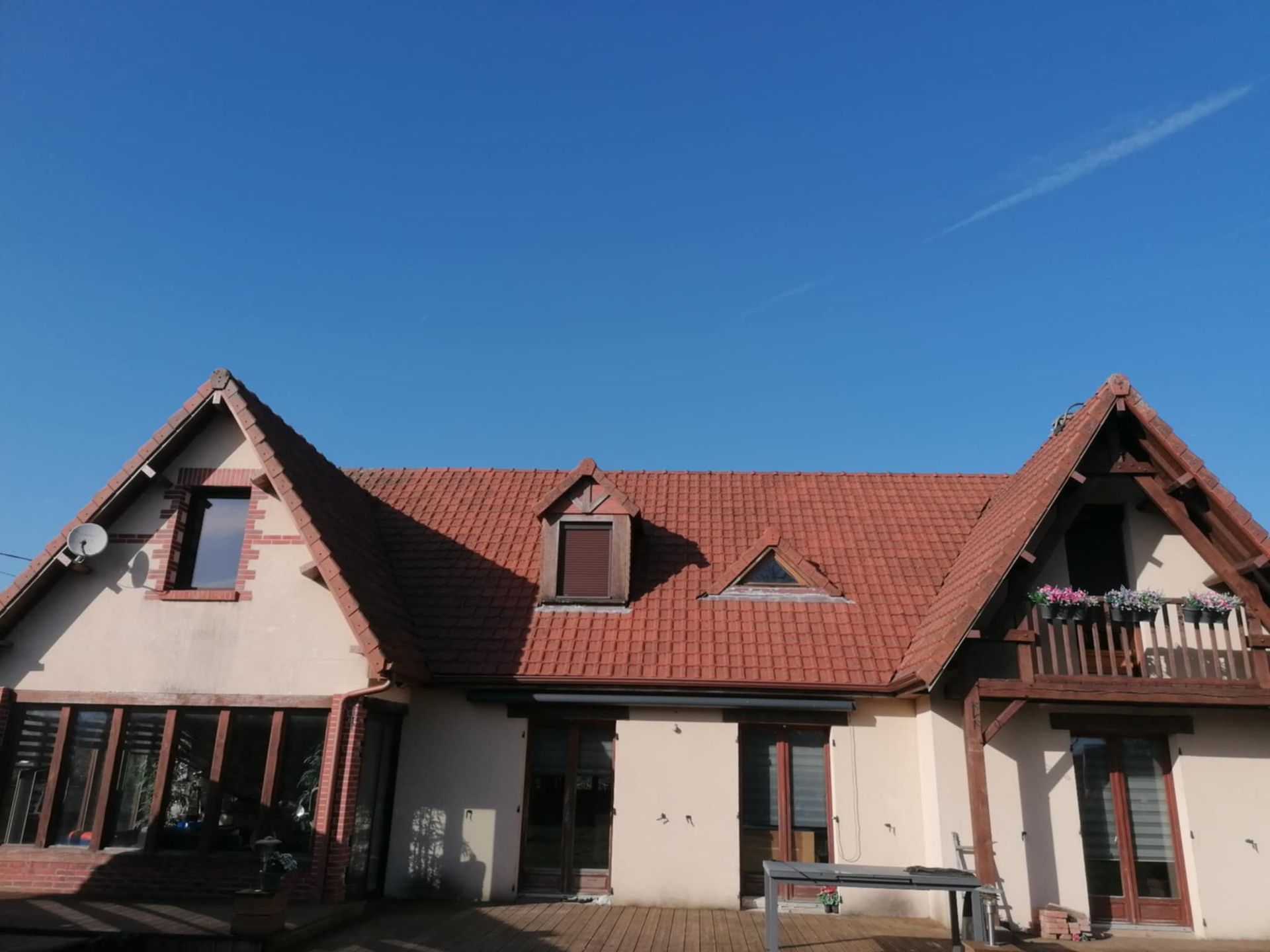 Maison beige au toit de tuiles rouges se détachant sur un ciel bleu. Elle présente un toit à pignons et des fenêtres.