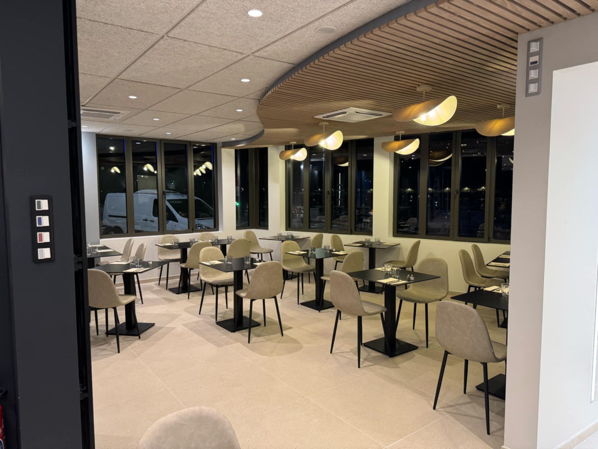 Intérieur du restaurant : tables et chaises, plafond incurvé avec éclairage, fenêtres avec vue sur la ville.