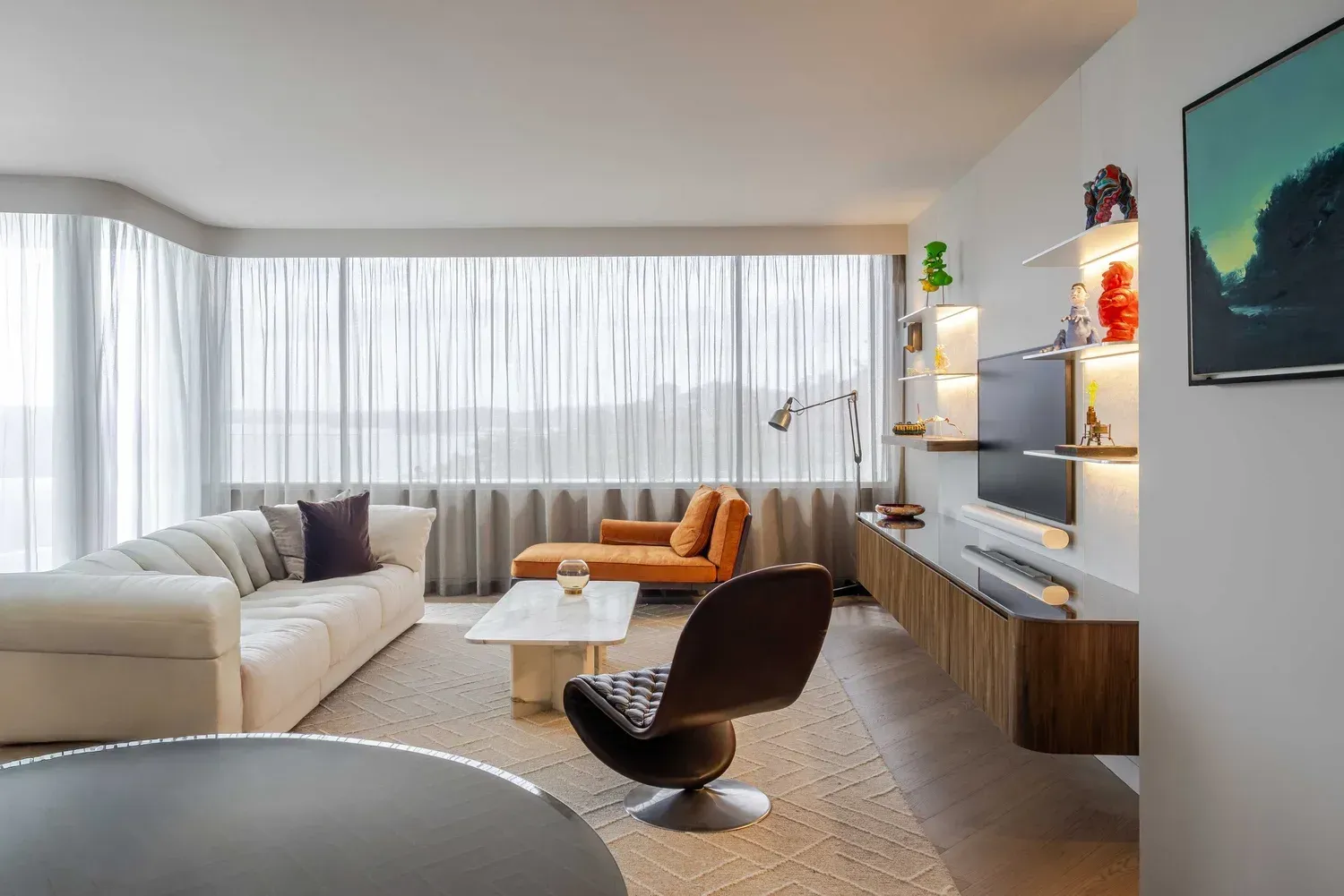Modern living room with white sofa, brown chair, large window, and wall-mounted TV on wooden console